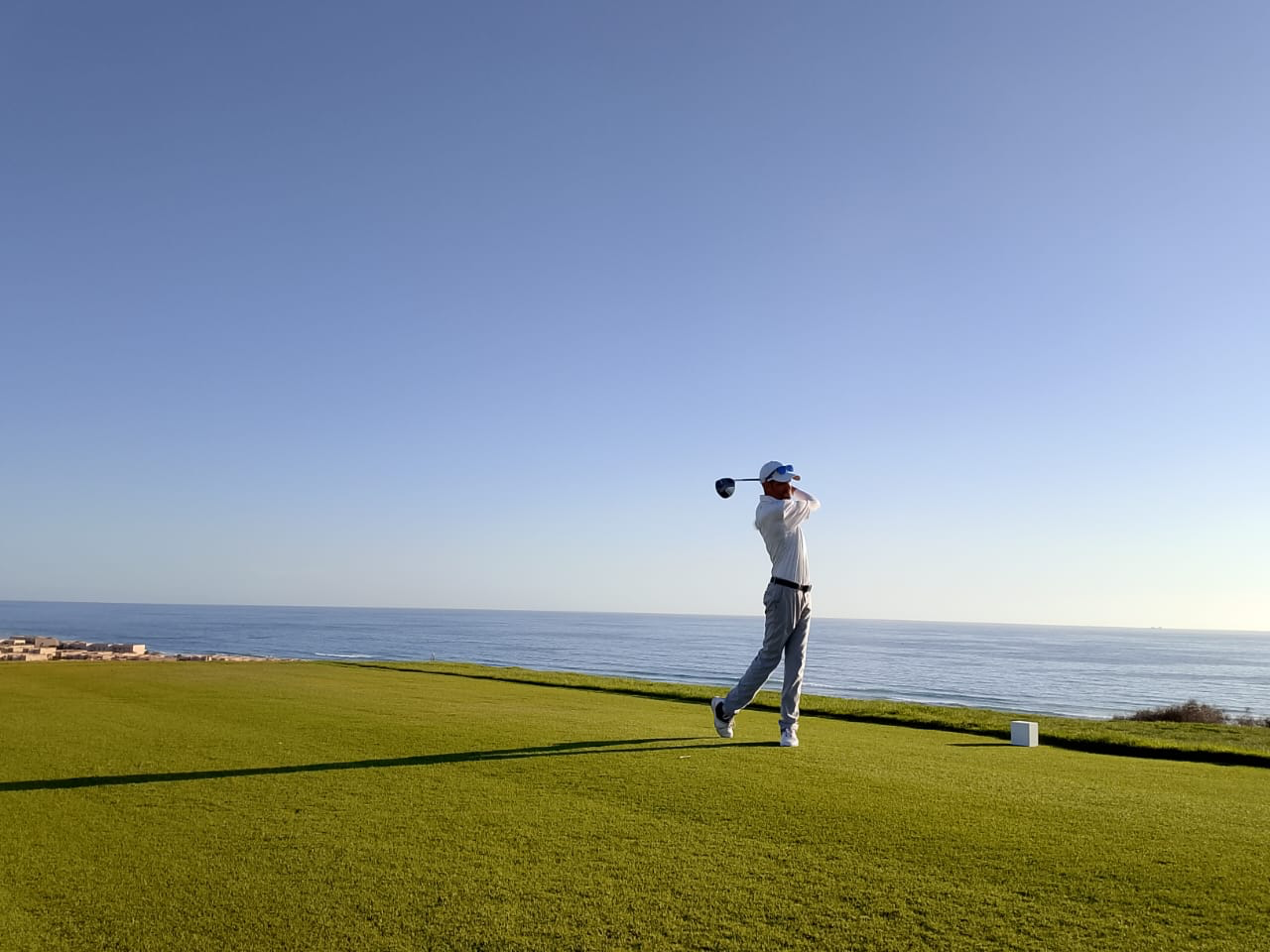 Golfer finishing a shot on a coastal golf course beside the sea